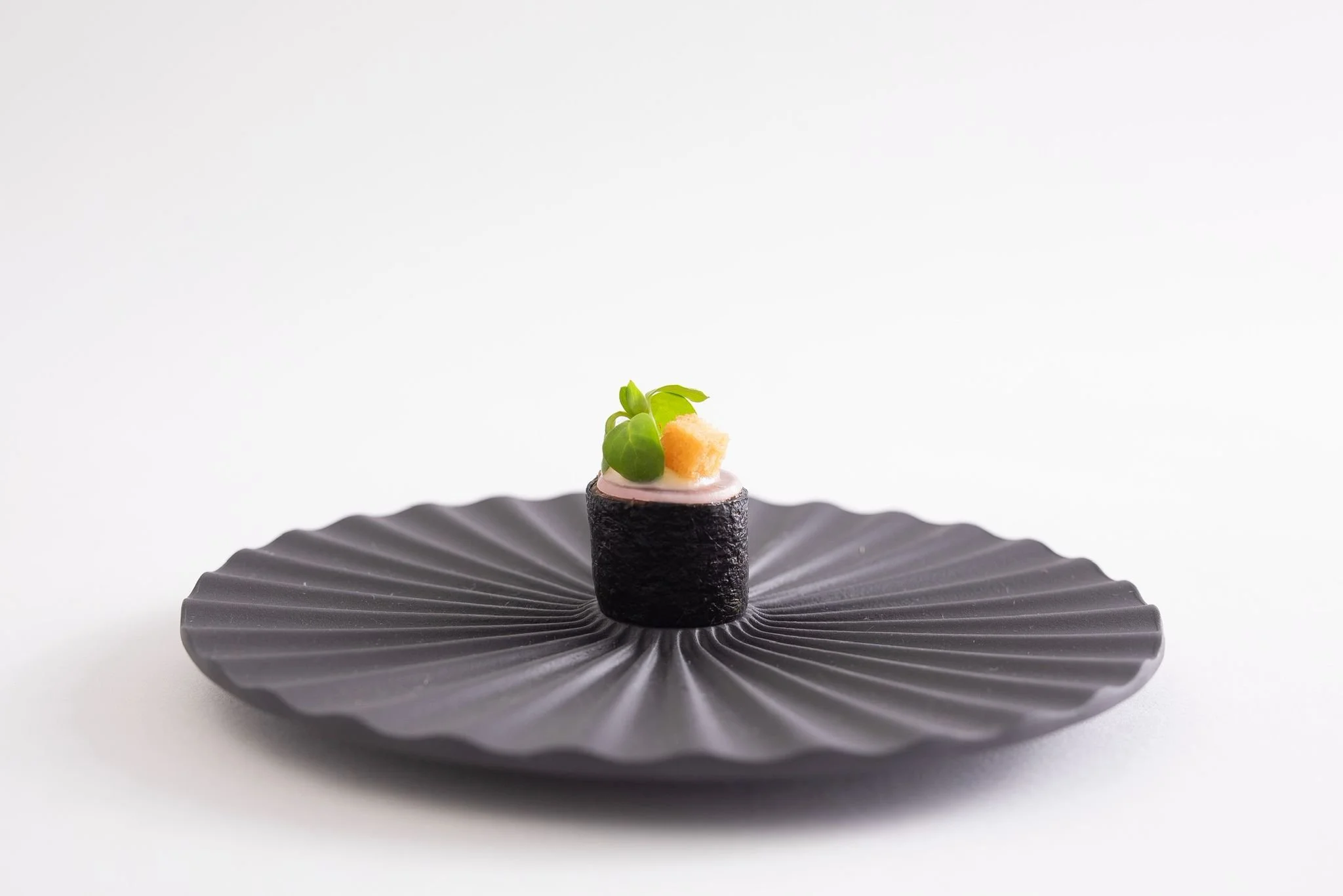 Un sushi noir avec de la garniture verte, du gingembre et de la sauce, présenté sur une assiette noire en forme de fleur.