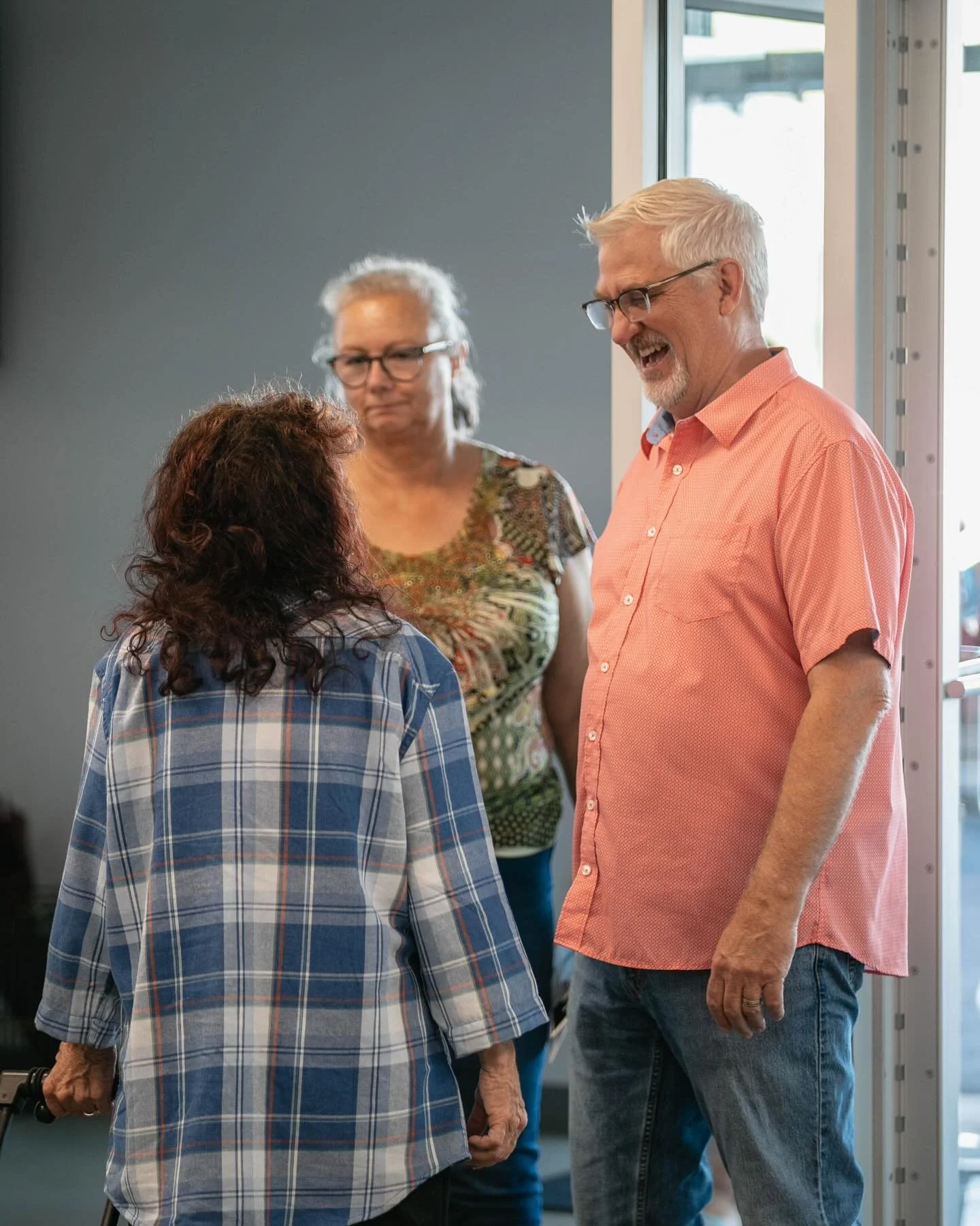 Three older adults having a conversation inside a room near a glass door.
