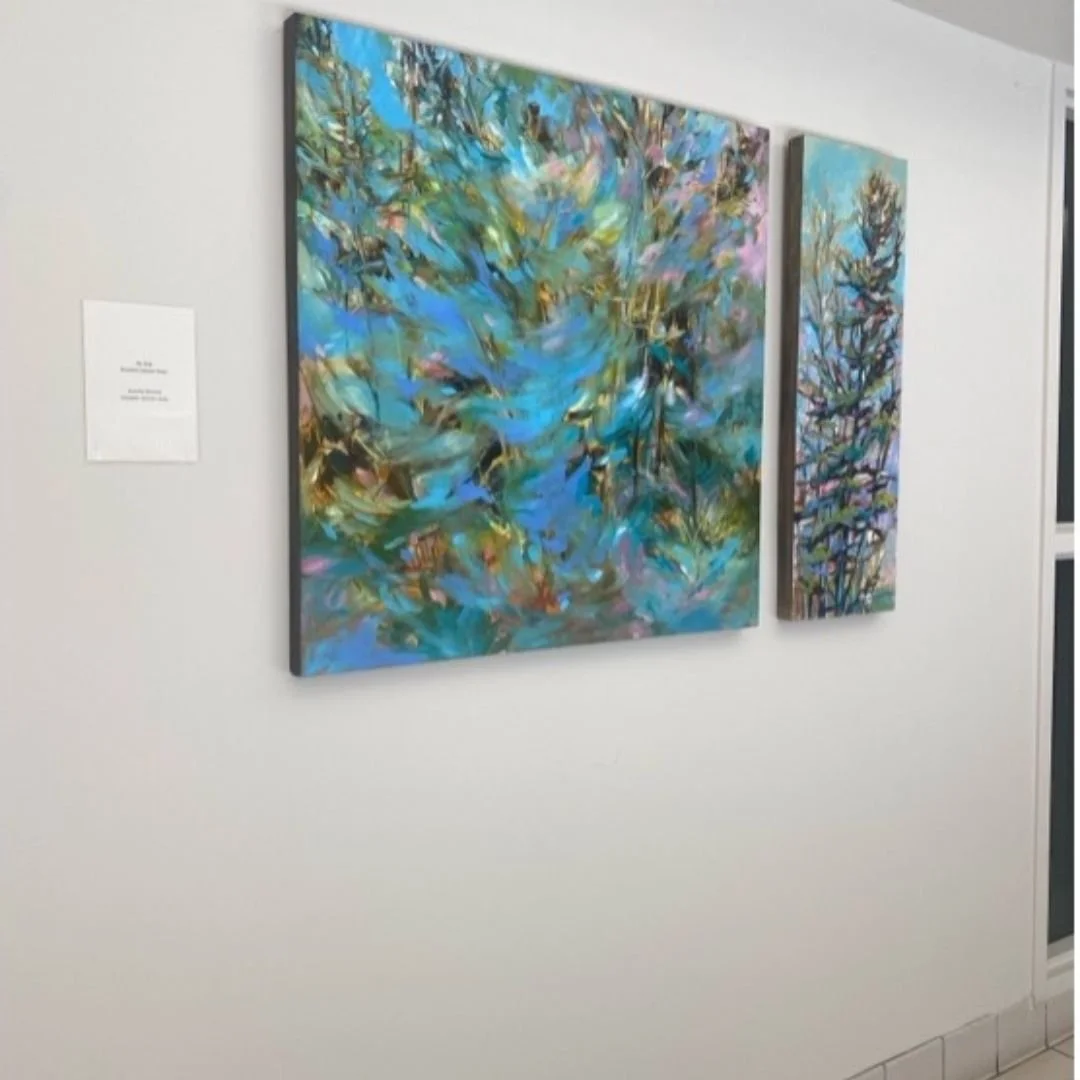 Two abstract paintings with shades of blue, purple, green, and gold hung on a white wall in an art gallery.