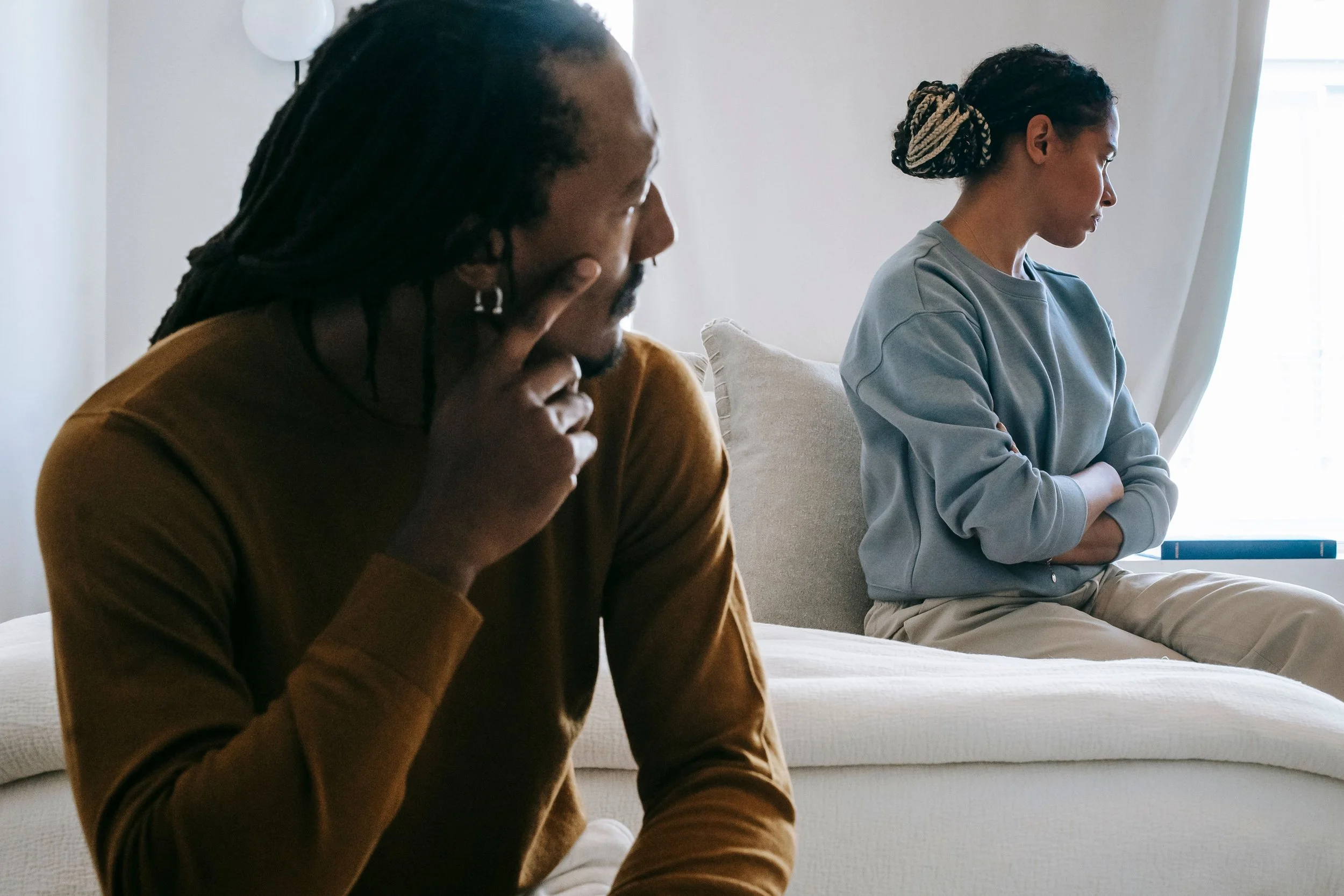 Couple sitting apart in bed, feeling alone while grieving miscarriage and pregnancy loss. Psychologist/Therapist specializing in miscarriage grief, perinatal mental health, relationship therapy, and couples therapy. Licensed in CA, FL, VA, TX, & ID.