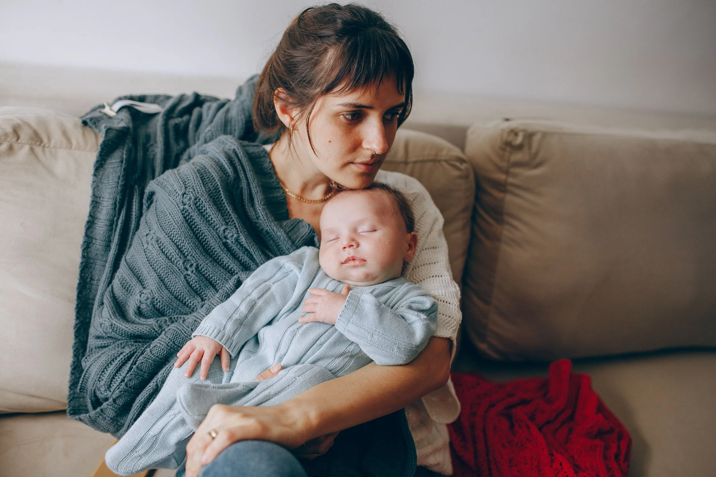 Woman who recently gave birth cradles her newborn looking exhausted and overwhelmed. image supporting evidence based virtual post partum therapy for orange county, LA, SF and california