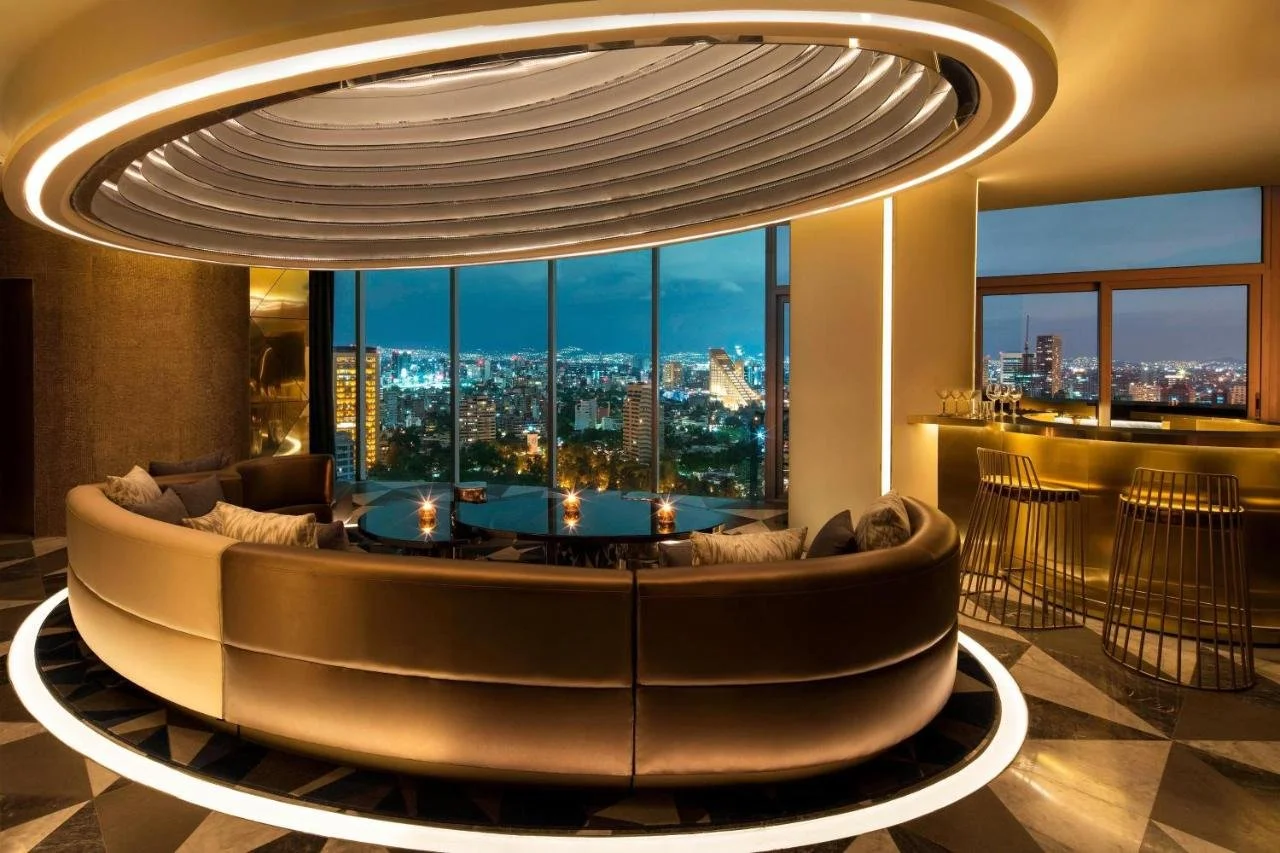 W Mexico City circular gold-lit lounge with curved leather banquette and floor-to-ceiling windows revealing Mexico City skyline and Chapultepec forest at night