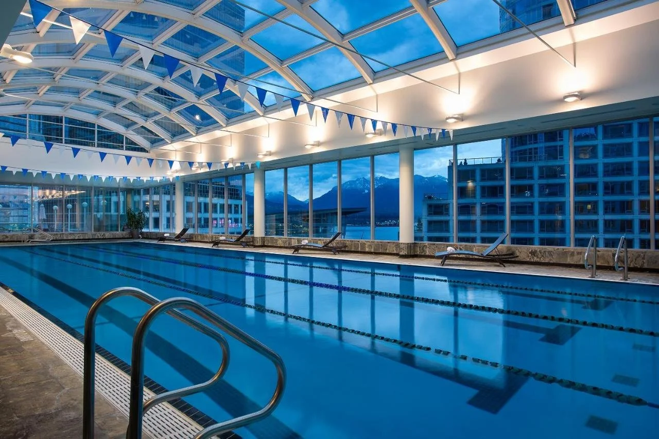 Auberge Vancouver Hotel indoor pool with glass ceiling and floor-to-ceiling windows showing Coal Harbour and snow-capped North Shore Mountains at dusk