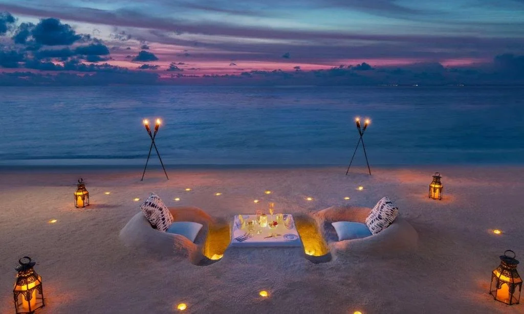 Waldorf Astoria Maldives Ithaafushi private beach dinner at dusk with sand-carved armchairs, Moroccan lanterns and torches facing the Indian Ocean at twilight