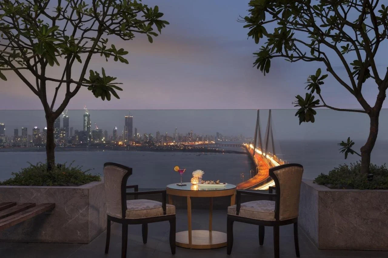Taj Lands End Mumbai rooftop terrace at dusk with the Bandra-Worli Sea Link lit up and the Mumbai skyline across the Arabian Sea