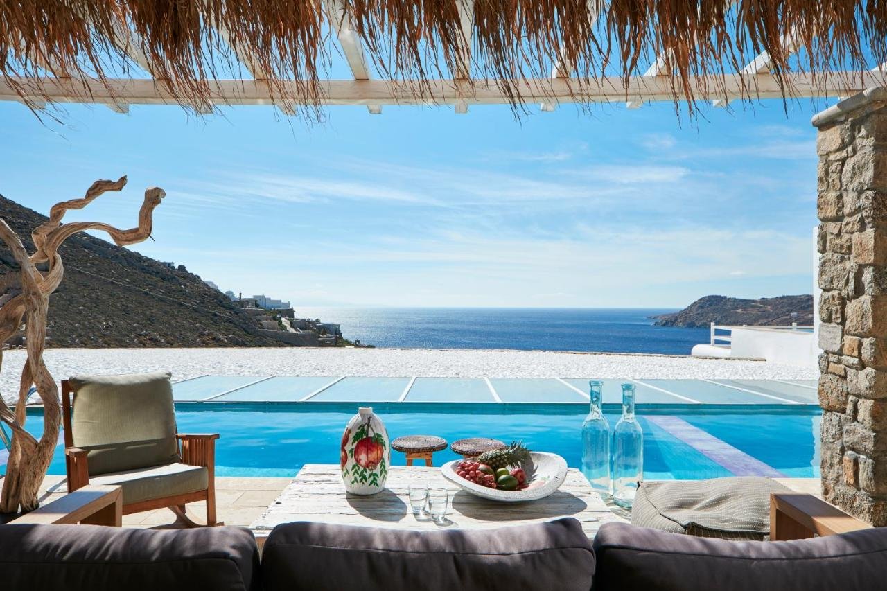 Myconian Villa Collection Mykonos thatched terrace with private infinity pool and Aegean Sea coastline and rocky hills