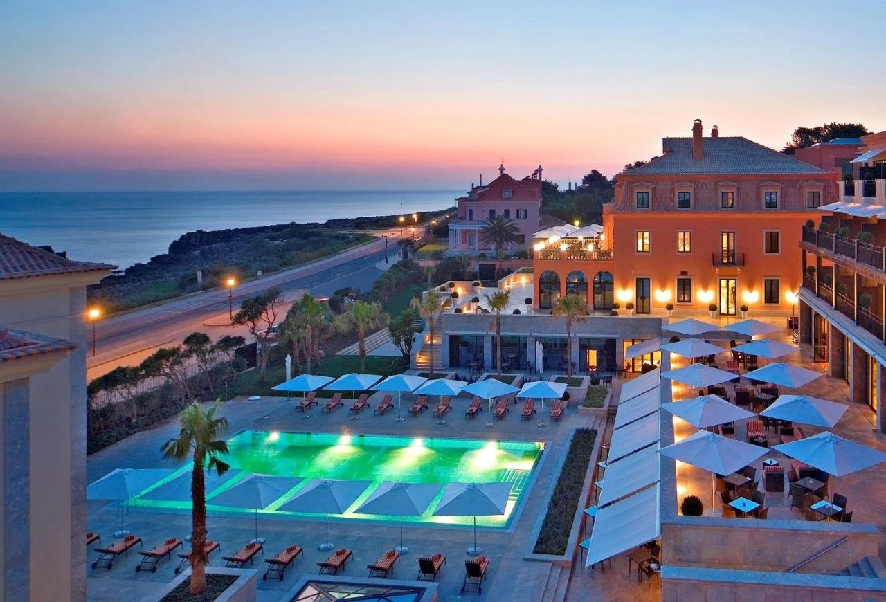 Grande Real Villa Itália Hotel & Spa Cascais aerial view at sunset with illuminated outdoor pool terrace and Atlantic Ocean