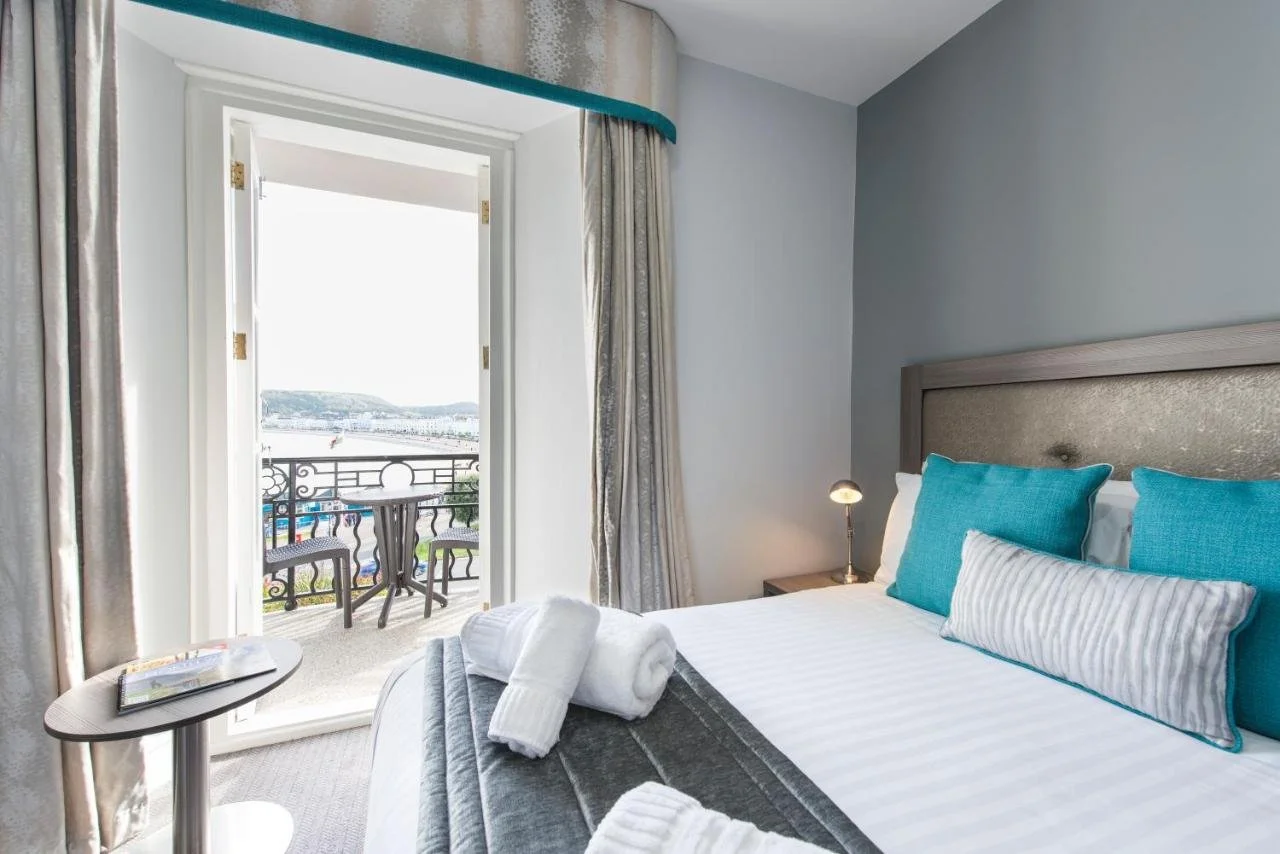 Belmont Llandudno hotel room with teal accents and French doors opening to iron balcony overlooking Llandudno Bay promenade