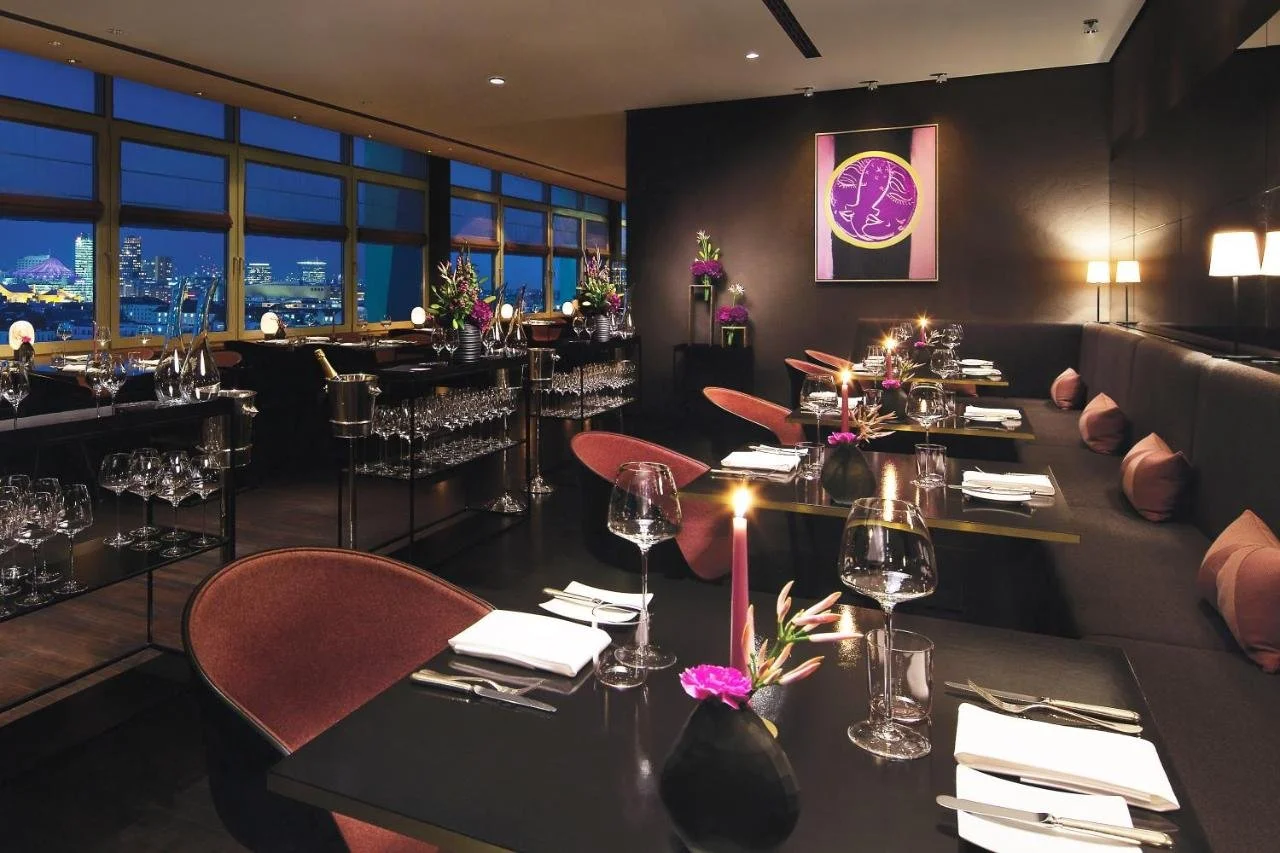 InterContinental Berlin Berlin Hugos restaurant darkly decorated dining room at night with candlelit tables and panoramic city skyline including the Sony Center tent roof through full-height windows