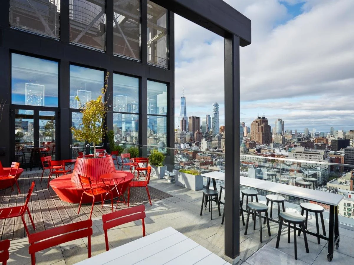 citizenM New York Bowery rooftop bar with red chairs and Lower Manhattan skyline including One World Trade Center