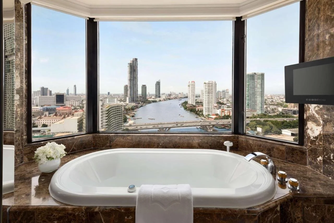 Shangri-La Bangkok suite marble bathroom with oval bathtub facing bay windows overlooking Chao Phraya River and skyline