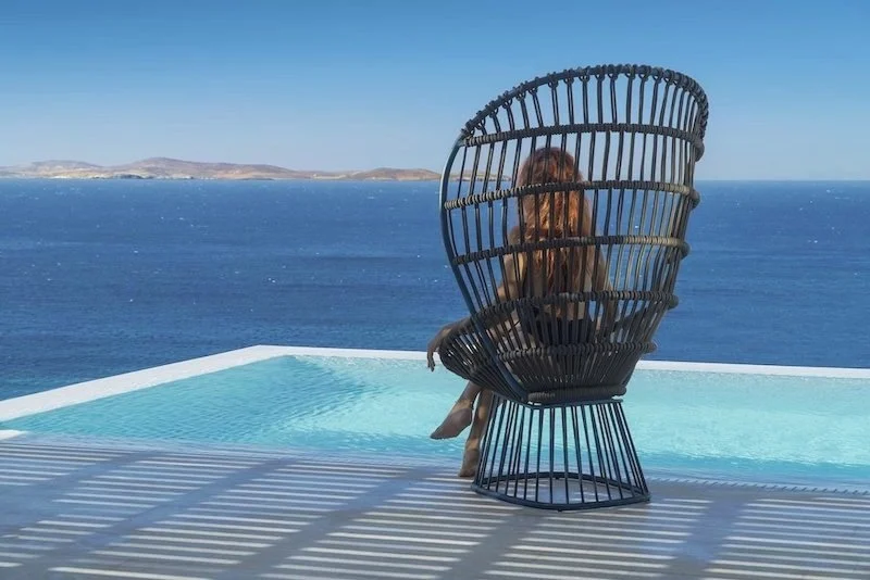 Mykonos Riviera Hotel & Spa Tourlos infinity pool terrace with wicker chair and open Aegean Sea view with island in distance