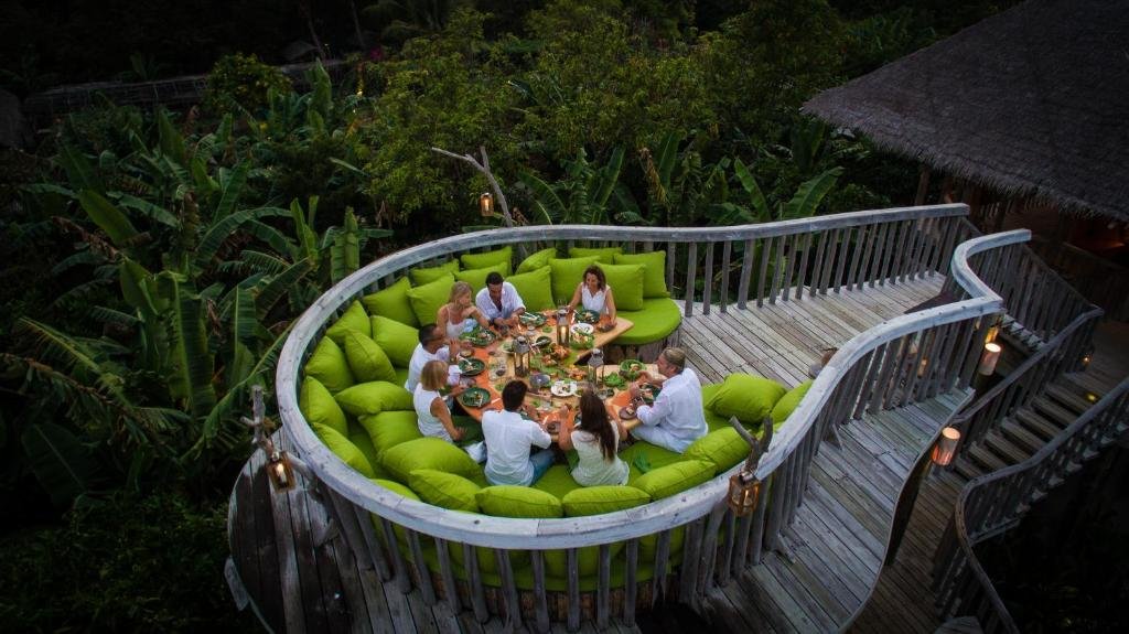 Soneva Fushi Maldives aerial view of circular treehouse dining deck with green banquette seating surrounded by tropical jungle canopy at dusk
