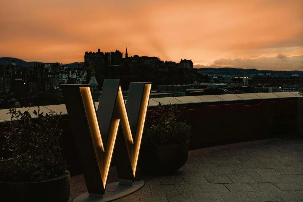W Edinburgh rooftop W Deck at sunset with illuminated W sign and Edinburgh Castle silhouette