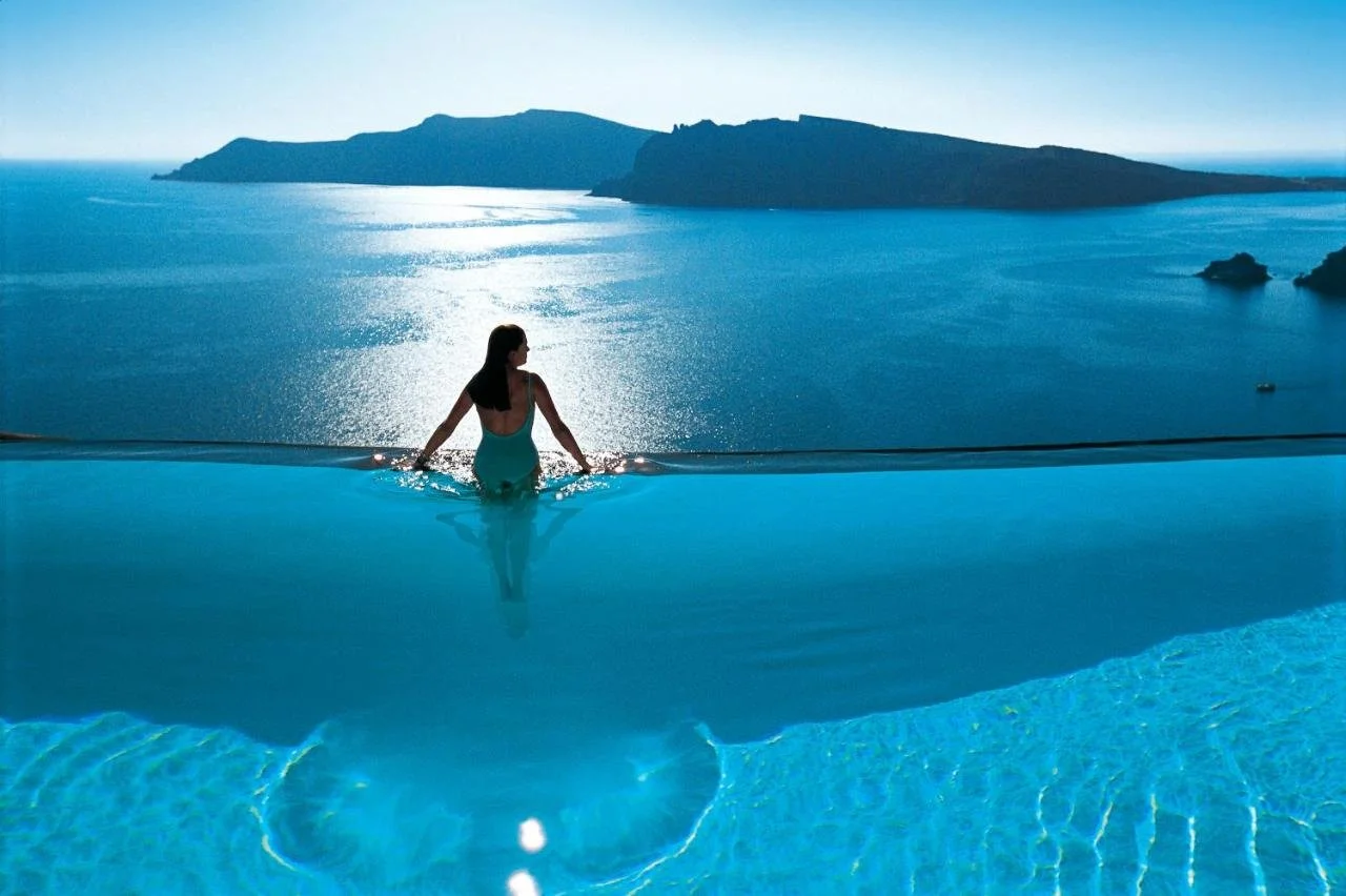 Perivolas Hotel Oia infinity pool with silhouetted figure facing caldera and Thirassia island