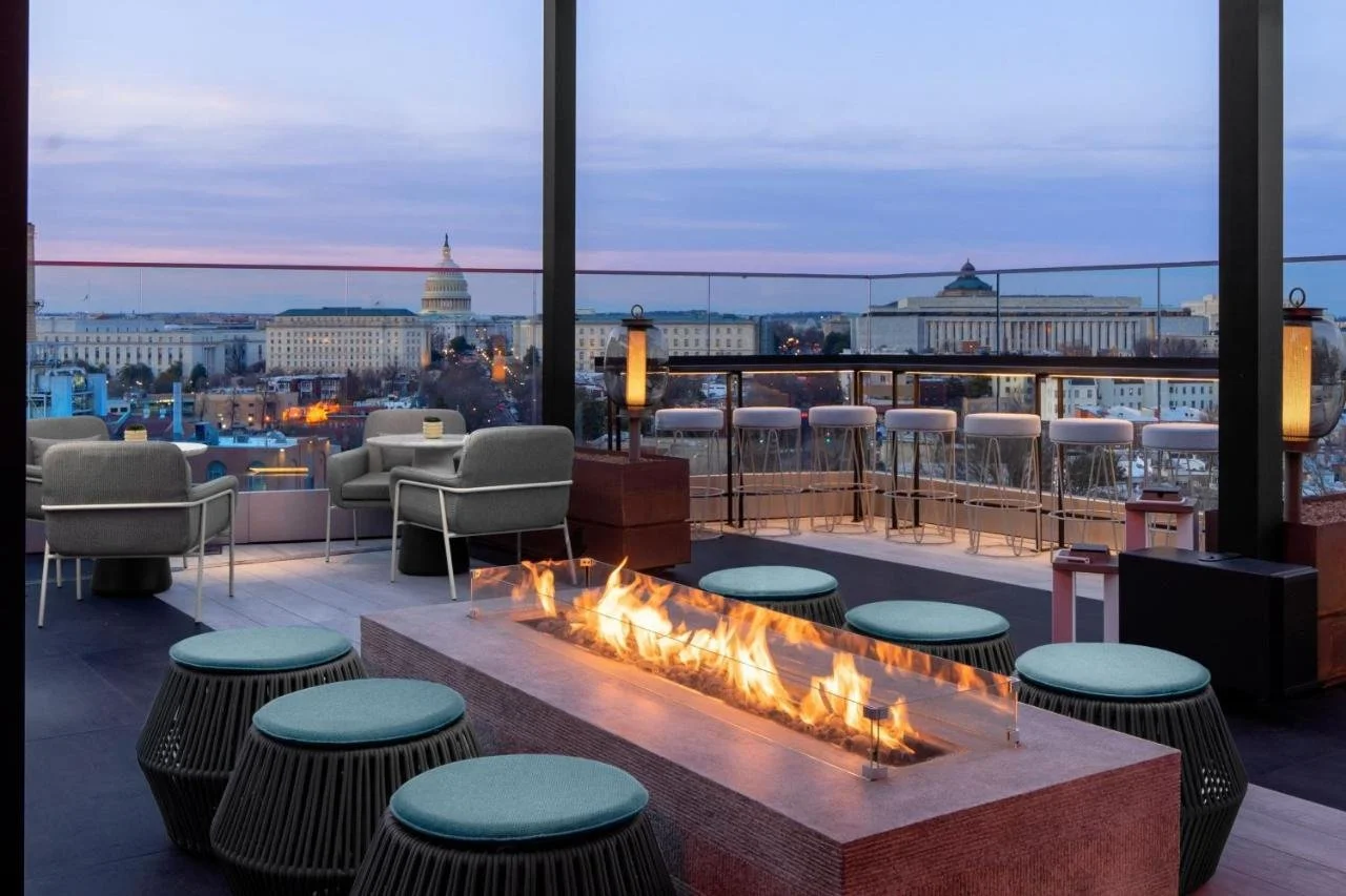 AC Hotel by Marriott Washington DC Capitol Hill Navy Yard rooftop terrace at dusk with a lit fire pit and bar stools, the illuminated U.S. Capitol dome filling the background