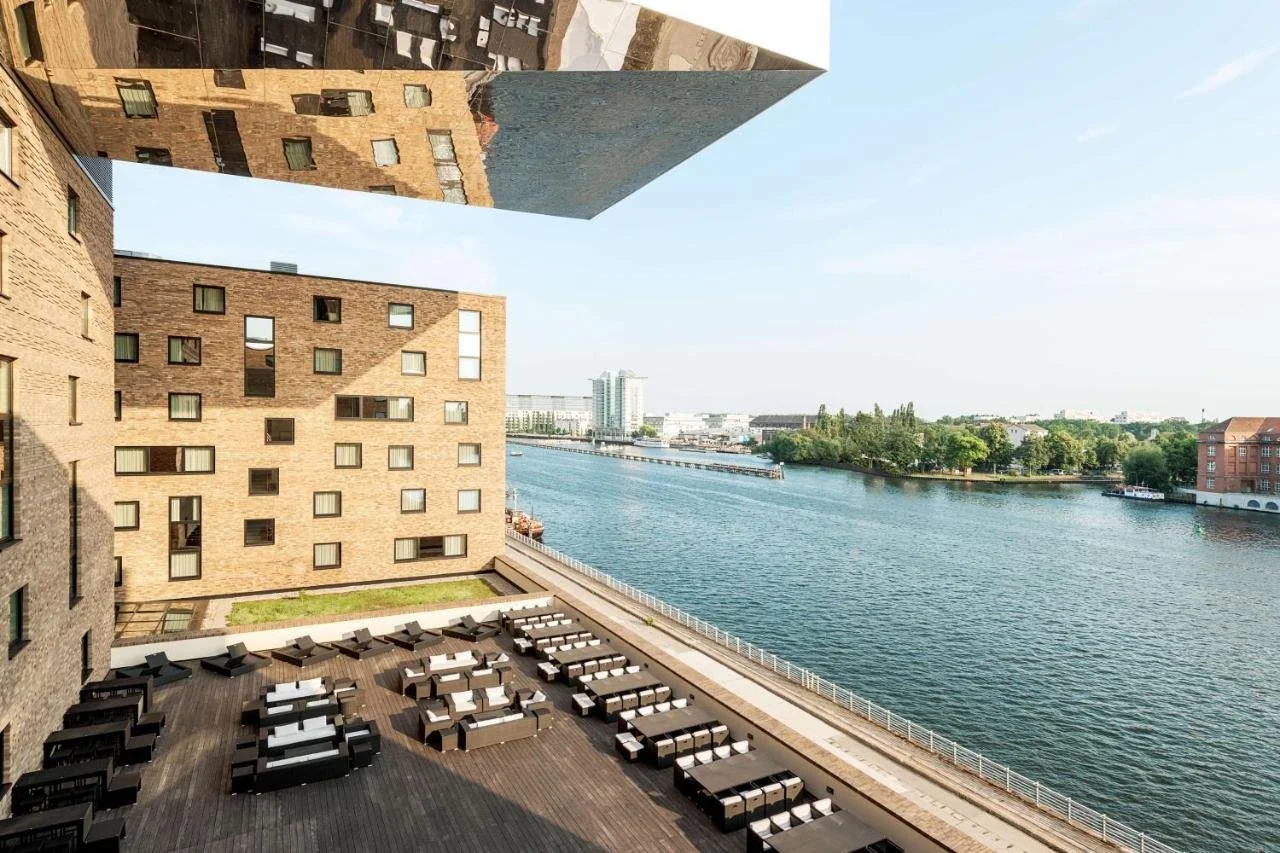 nhow Berlin Berlin aerial view of the hotel's mirrored cantilevered volume over the riverside terrace and the Spree River with the opposite bank and city skyline beyond