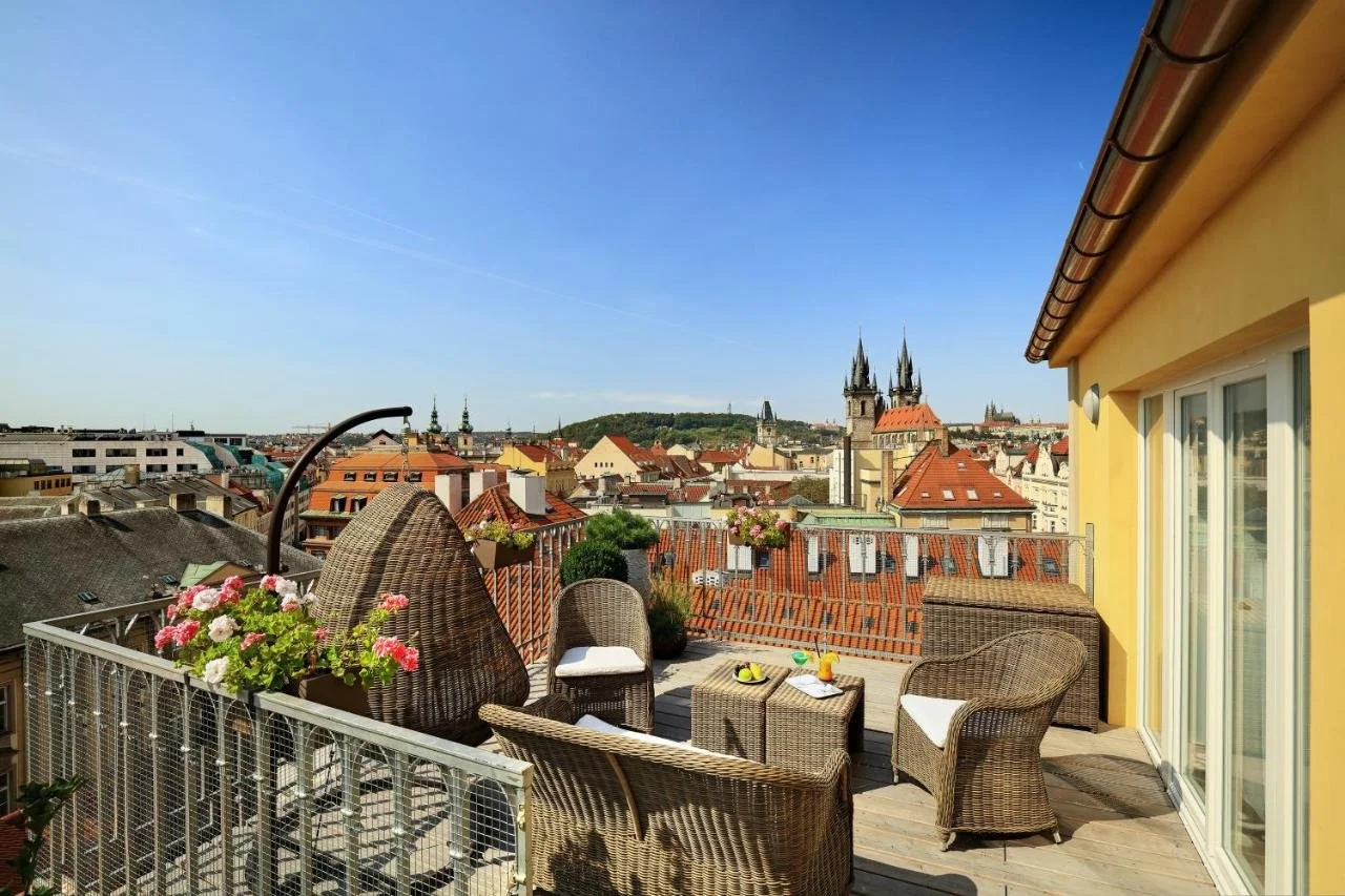 Grand Hotel Bohemia Prague rooftop terrace with rattan furniture and red Old Town rooftops, Týn Church twin Gothic towers prominent to the left