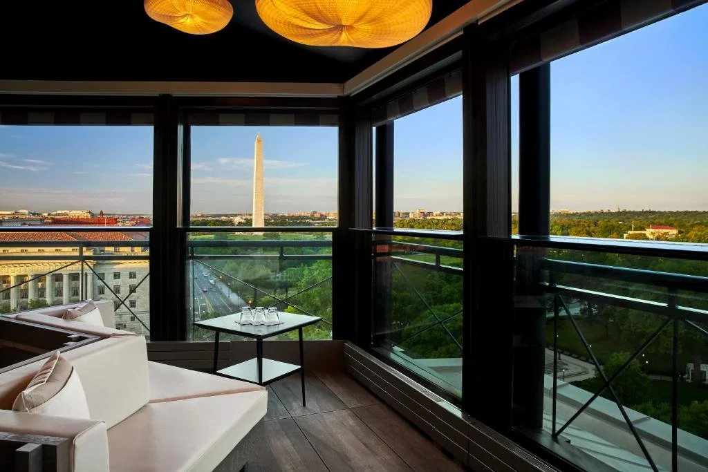 Hotel Washington Washington DC enclosed rooftop terrace with rattan ceiling pendants, the Washington Monument seen through wraparound glass windows at golden hour