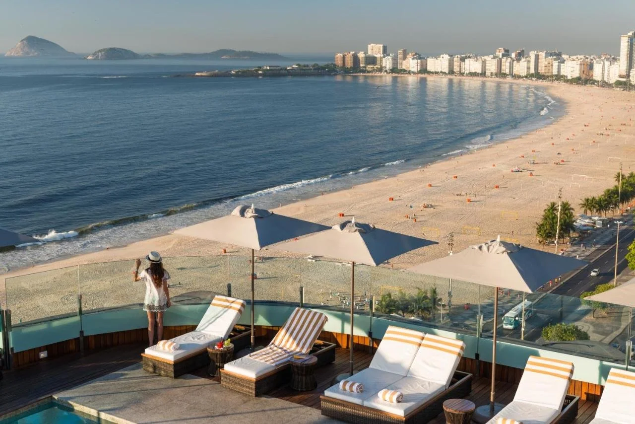 PortoBay Rio de Janeiro rooftop pool terrace with sun loungers overlooking Copacabana Beach and Cagarras Islands at sunset