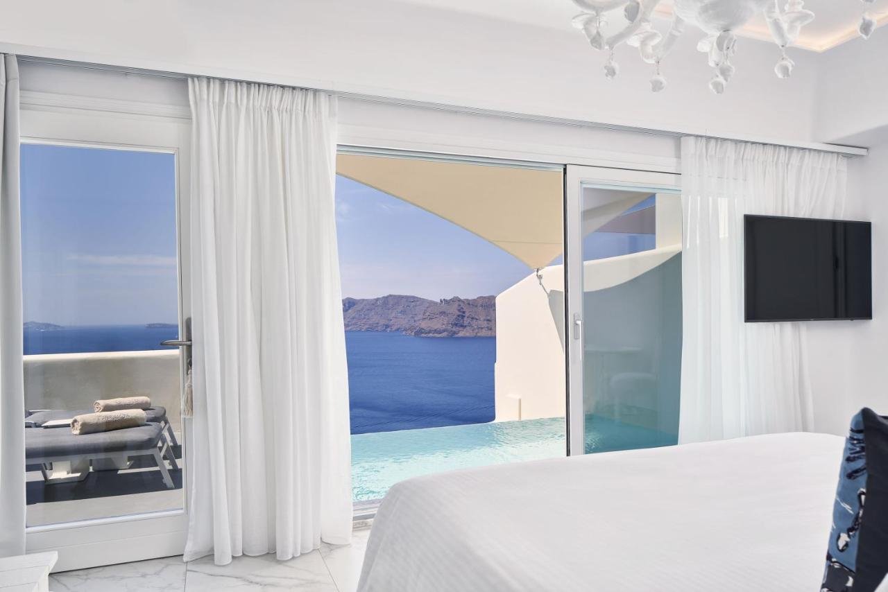 Canaves Oia Suites Oia bright suite interior with floor-to-ceiling windows opening to private pool and caldera