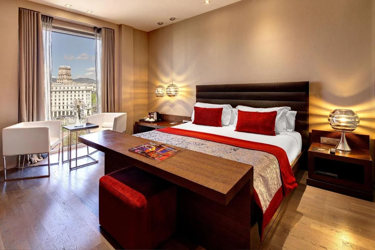 Olivia Plaza Hotel Barcelona hotel room with dark wood furniture and window view of a neoclassical building on Plaça de Catalunya with Tibidabo in the background