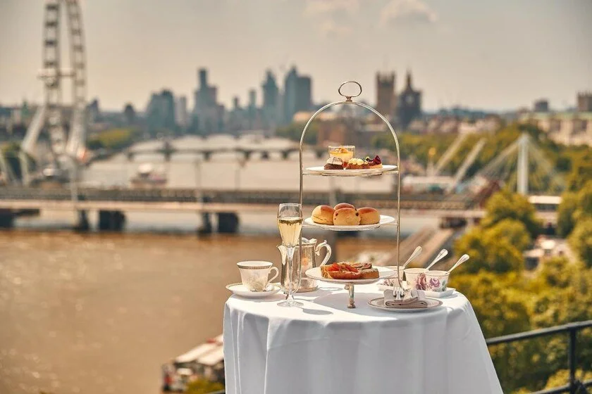 The Savoy London afternoon tea table set with silverware and views of the Thames, London Eye and Big Ben