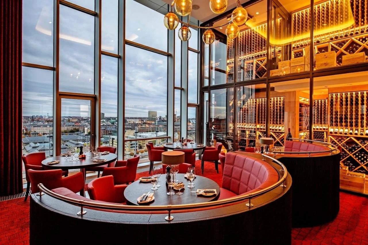 Tivoli Hotel Copenhagen restaurant with double-height floor-to-ceiling windows overlooking Copenhagen skyline at dusk and wine wall