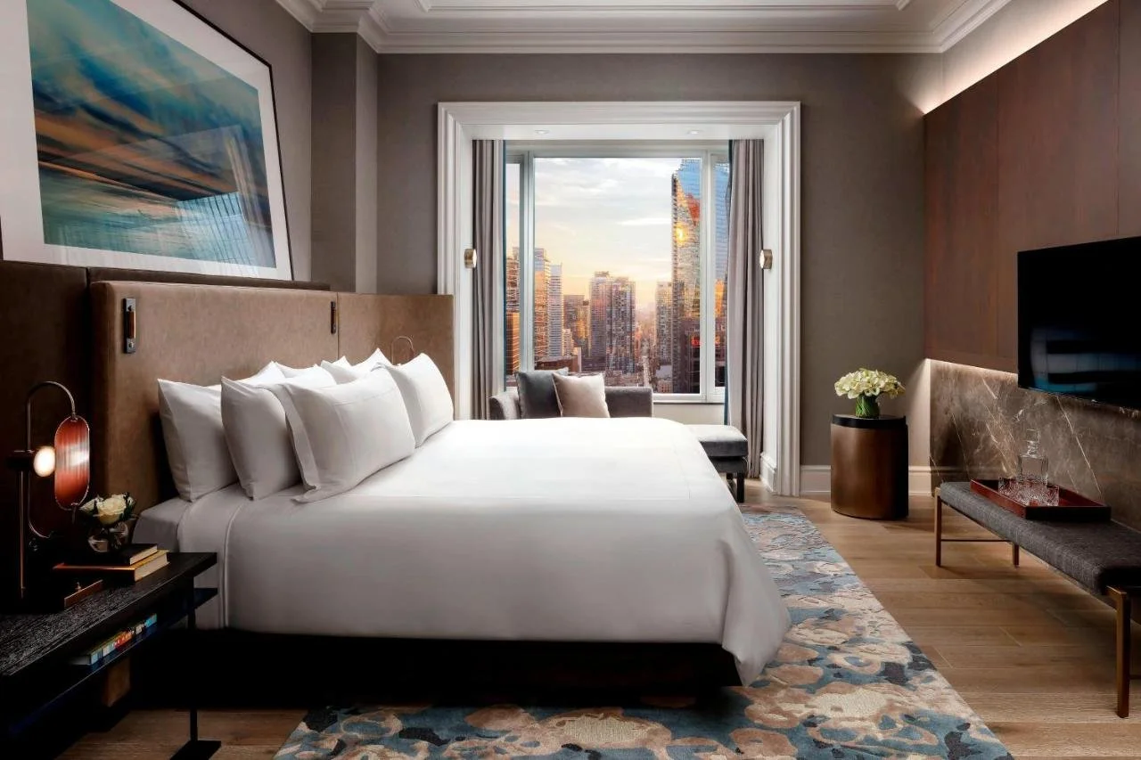 The St. Regis Toronto guest room with king bed and arched window overlooking Toronto skyscrapers bathed in golden sunset light