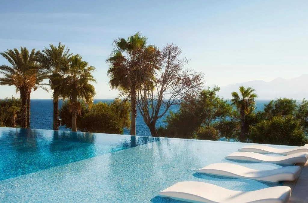 Akra Hotel Antalya infinity pool bordered by palm trees with Mediterranean Sea and Taurus Mountains at golden hour
