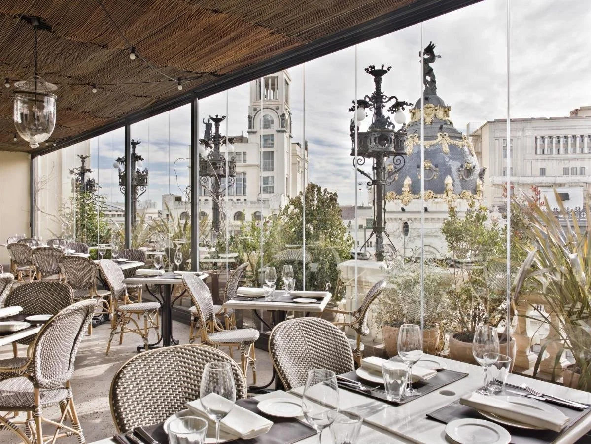 The Principal Madrid rooftop restaurant with glass walls framing the Metrópolis Building dome and ornate Gran Vía lampposts