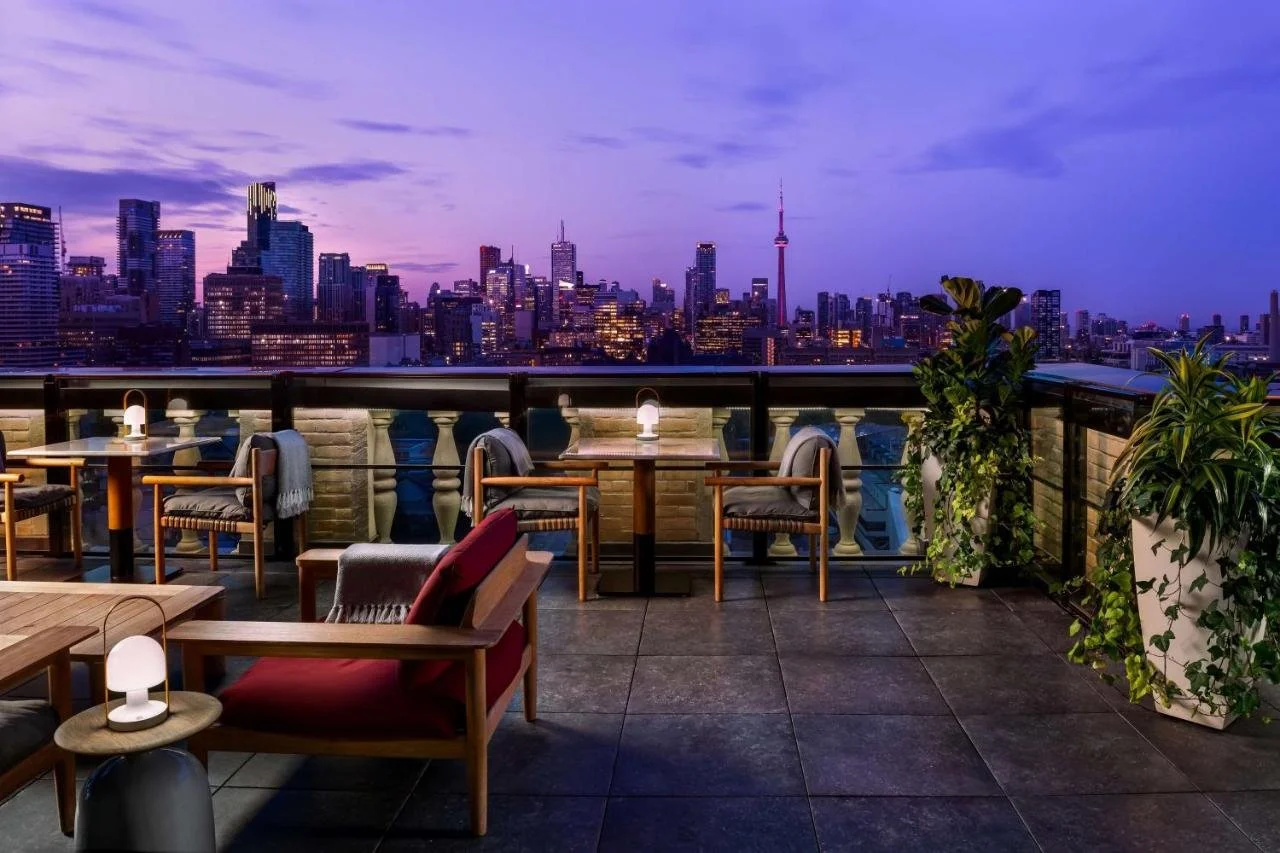 Park Hyatt Toronto Writers Room rooftop bar terrace at twilight with lounge chairs, lanterns, and the Toronto skyline with an illuminated CN Tower against a violet dusk sky