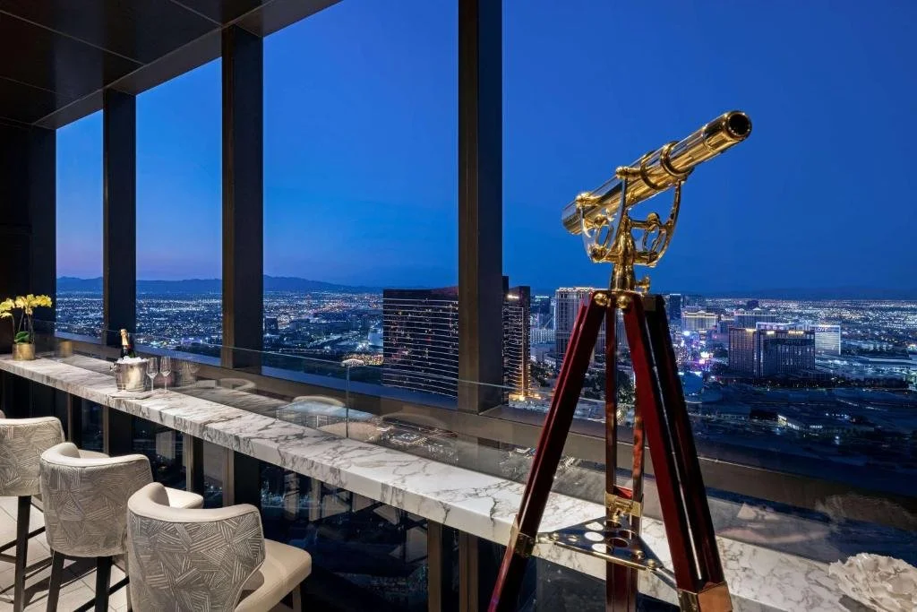 Crockfords Las Vegas LXR Hotels high-floor bar with marble counter and brass telescope overlooking the Strip and mountains at night