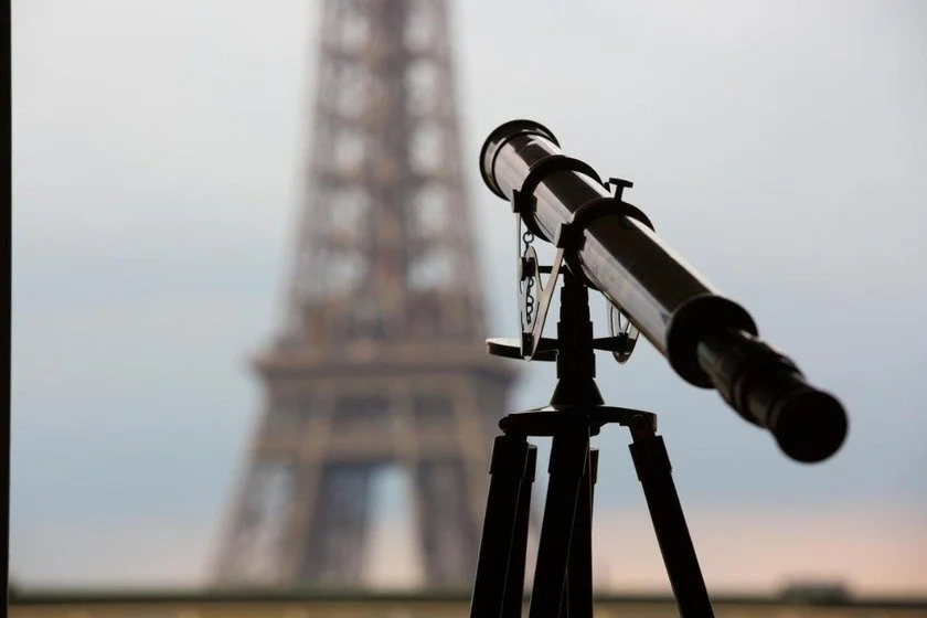 Eiffel Trocadéro Paris vintage brass telescope in the foreground, the Eiffel Tower softly blurred through the hotel window behind it