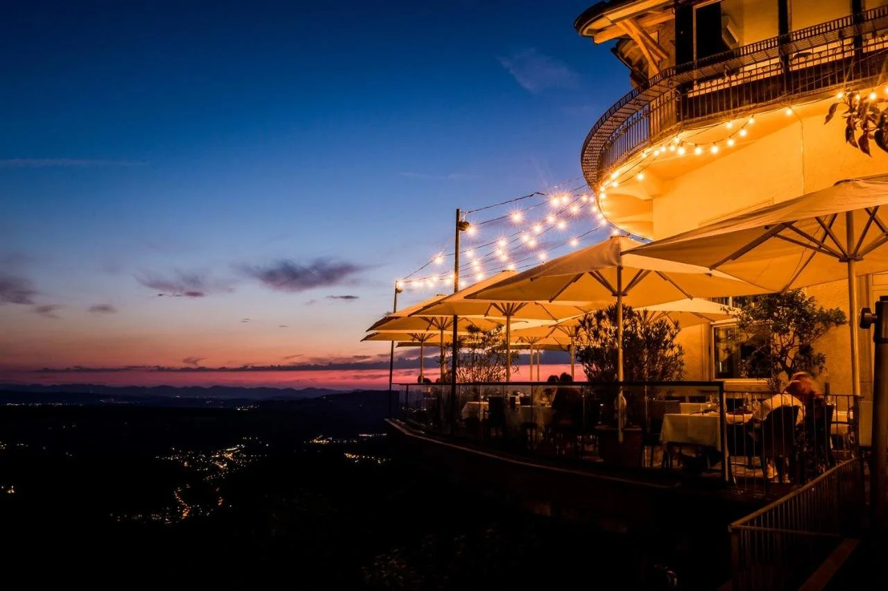 Hotel UTO KULM Zurich restaurant terrace with string lights at dusk, city lights spreading across the valley below at sunset