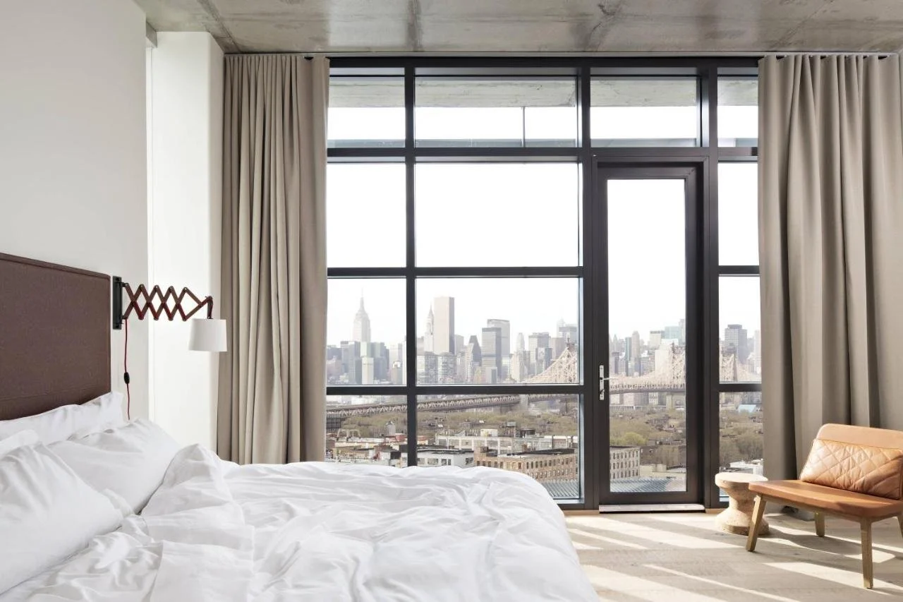 Boro Hotel Long Island City room with floor-to-ceiling windows overlooking Manhattan skyline with Empire State Building and Queensboro Bridge