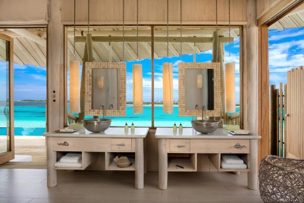 Soneva Jani Maldives open-air villa bathroom with double wooden vanity and woven mirrors, turquoise lagoon visible through open timber-frame walls