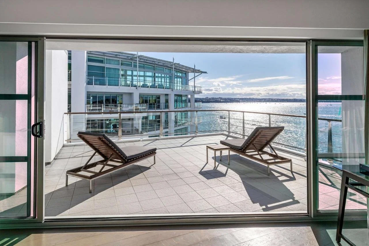Hilton Auckland Auckland suite terrace with two sun loungers facing the open Waitematā Harbour and the North Shore hills beyond
