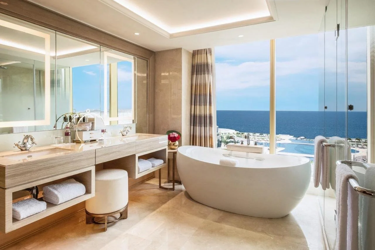 Okada Manila Manila marble suite bathroom with freestanding oval bathtub facing floor-to-ceiling windows overlooking the outdoor resort pool and Manila Bay
