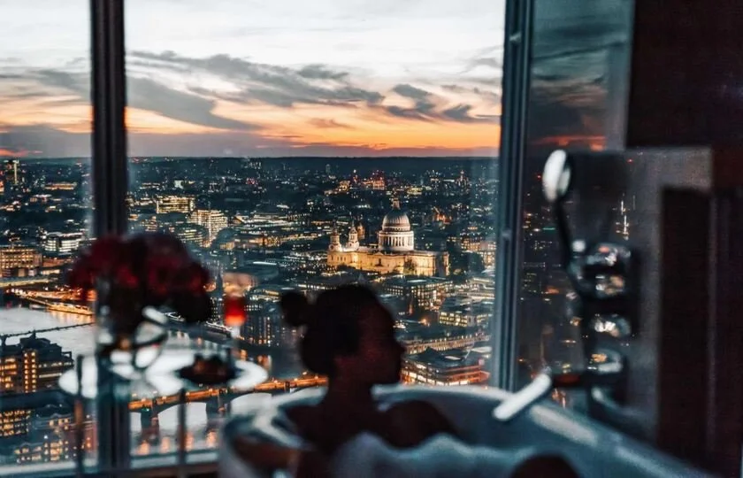 Shangri-La The Shard London woman bathing in suite with aerial panoramic night view including the river