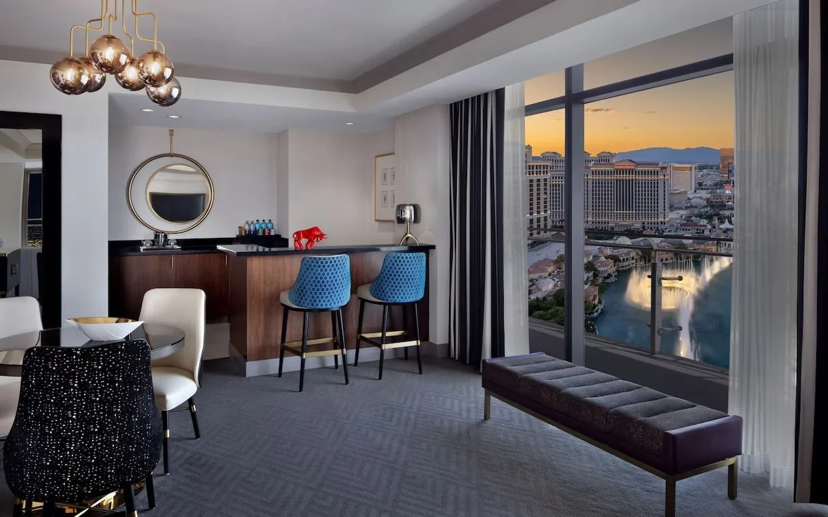 The Cosmopolitan of Las Vegas suite living area with window view of the Bellagio fountains and Strip at golden hour
