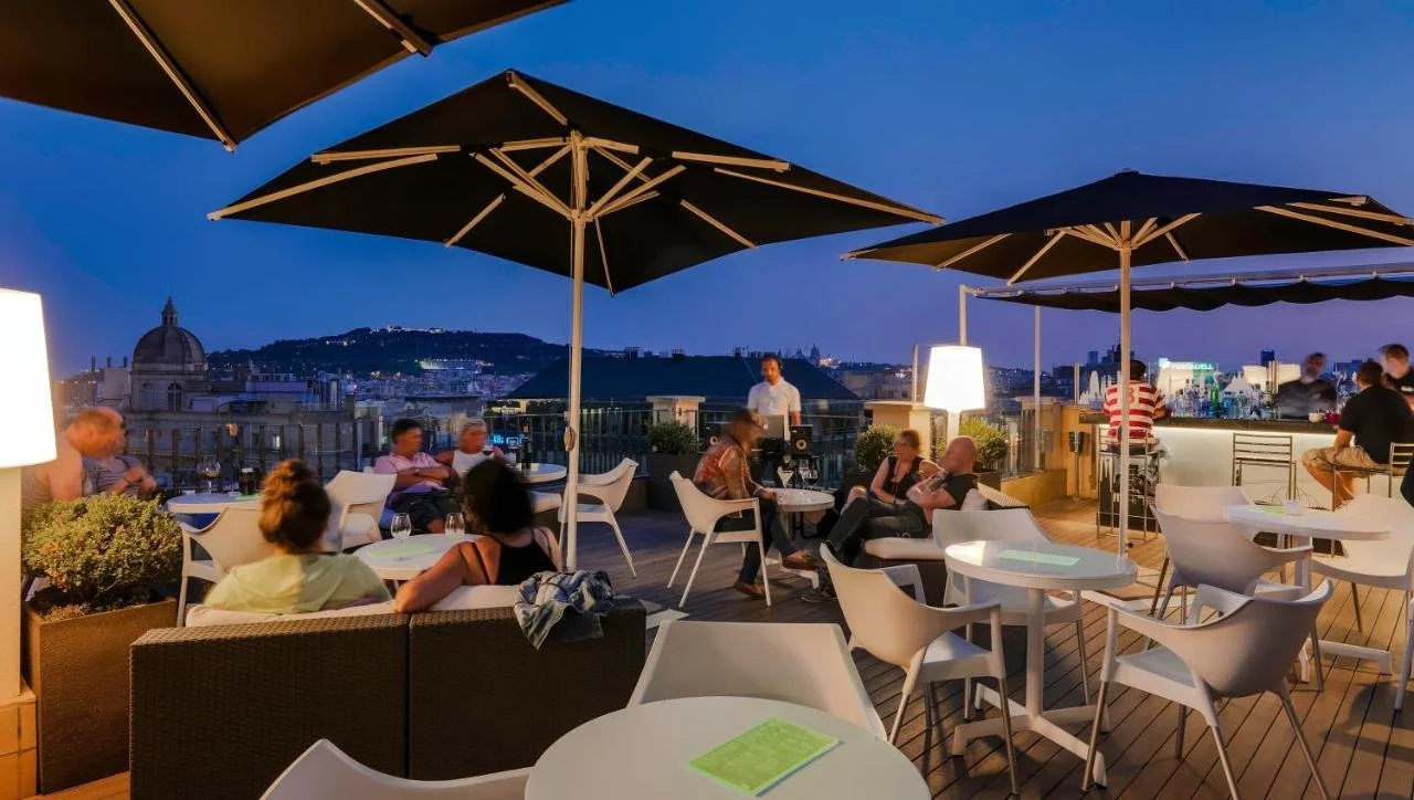 H10 Universitat Barcelona Twenty One rooftop terrace bar at dusk with Montjuïc hill and Palau Nacional in the background