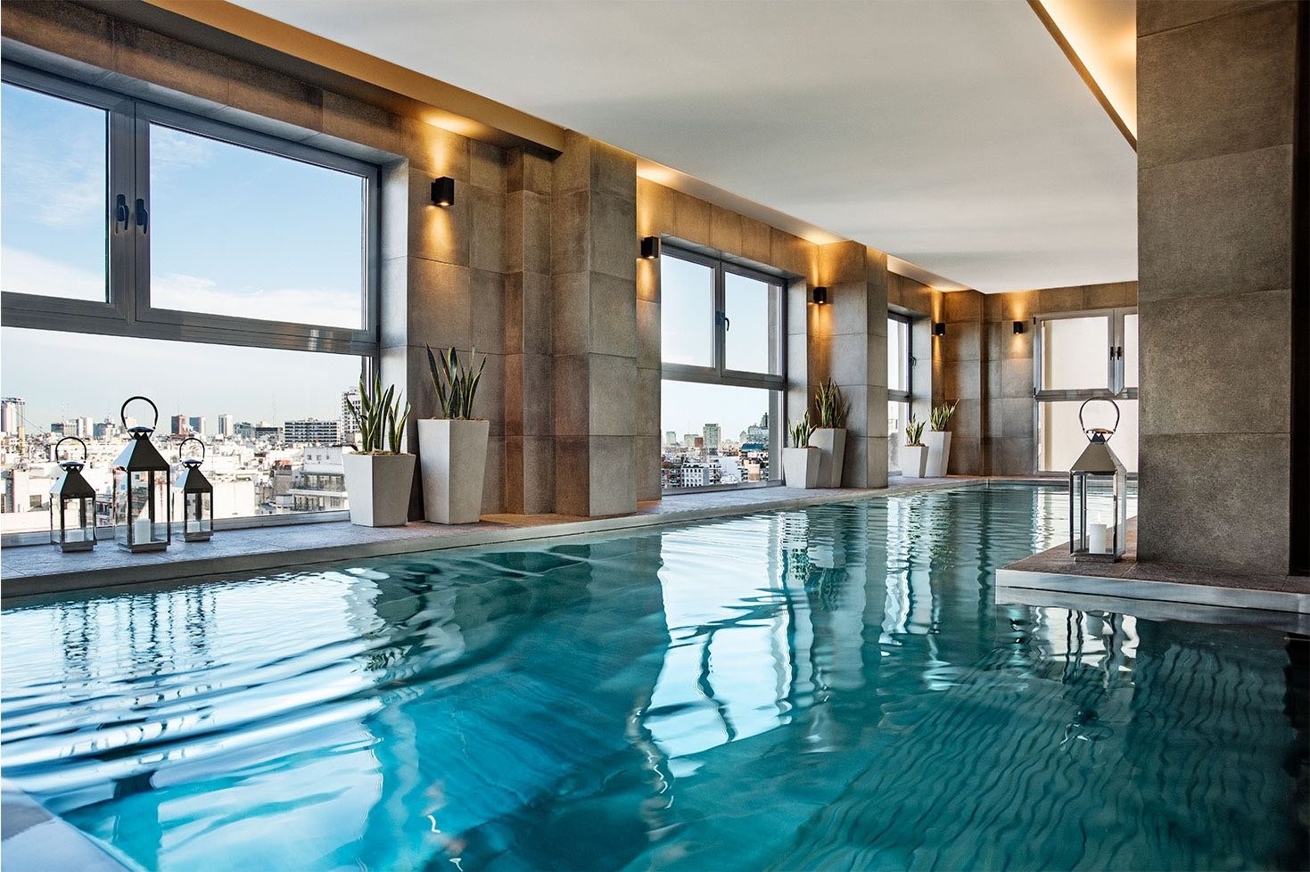 Alvear Palace Hotel Buenos Aires indoor rooftop pool with travertine walls, amber lighting, lantern décor, and Buenos Aires skyline visible through side windows