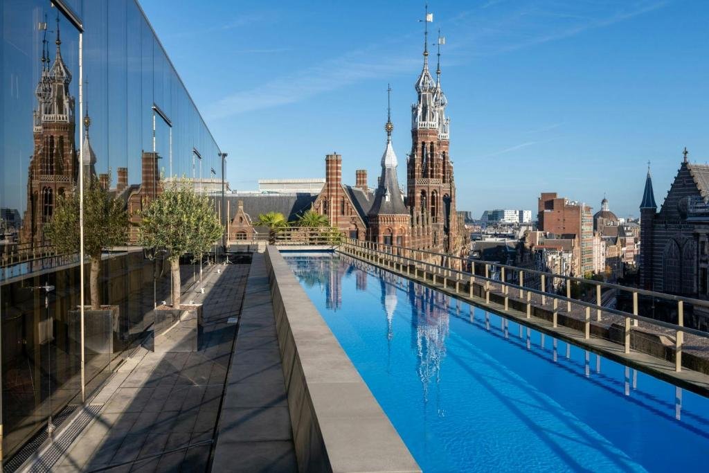 W Amsterdam WET Deck rooftop pool with olive trees and panoramic view of Amsterdam Gothic church spires and city skyline