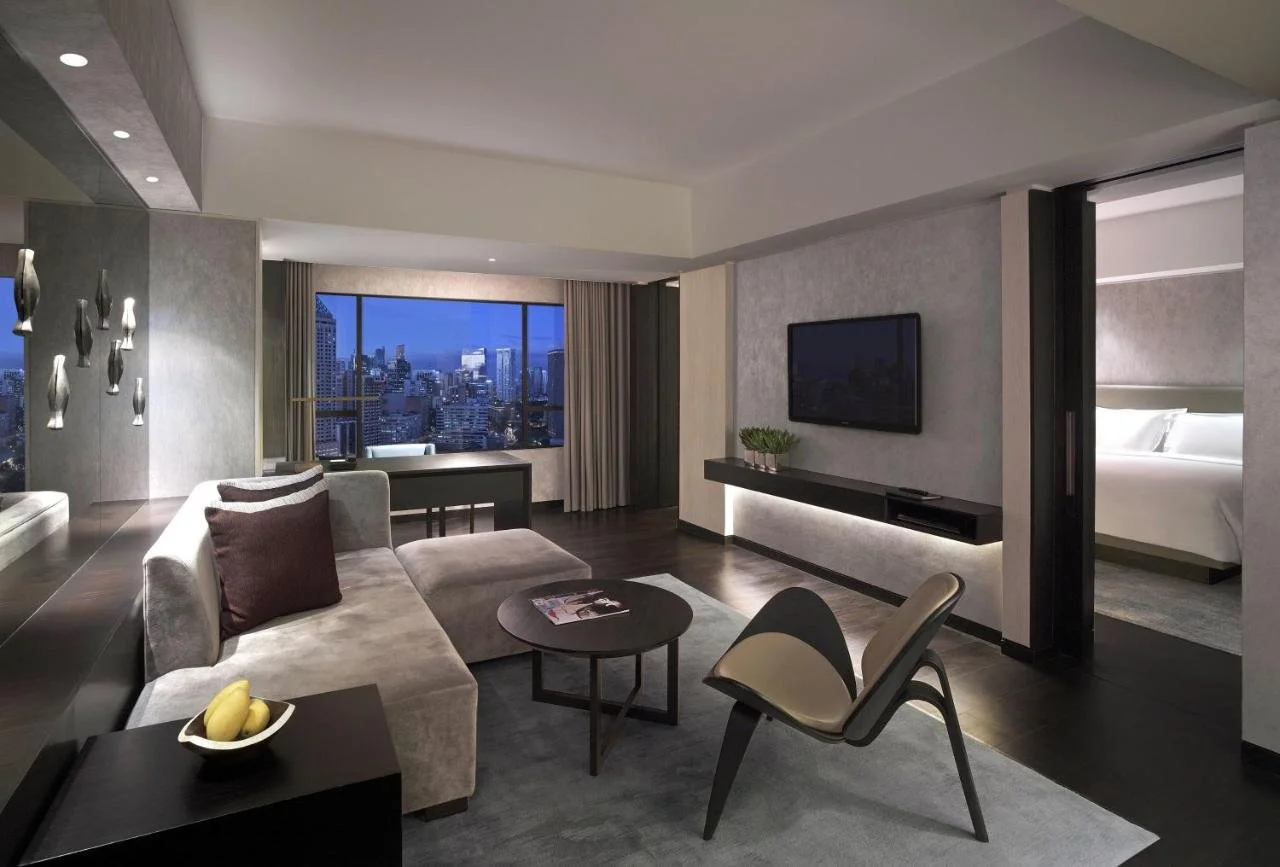 New World Makati Hotel Manila contemporary suite living area with large window framing the Makati skyline at dusk and bedroom visible through sliding door