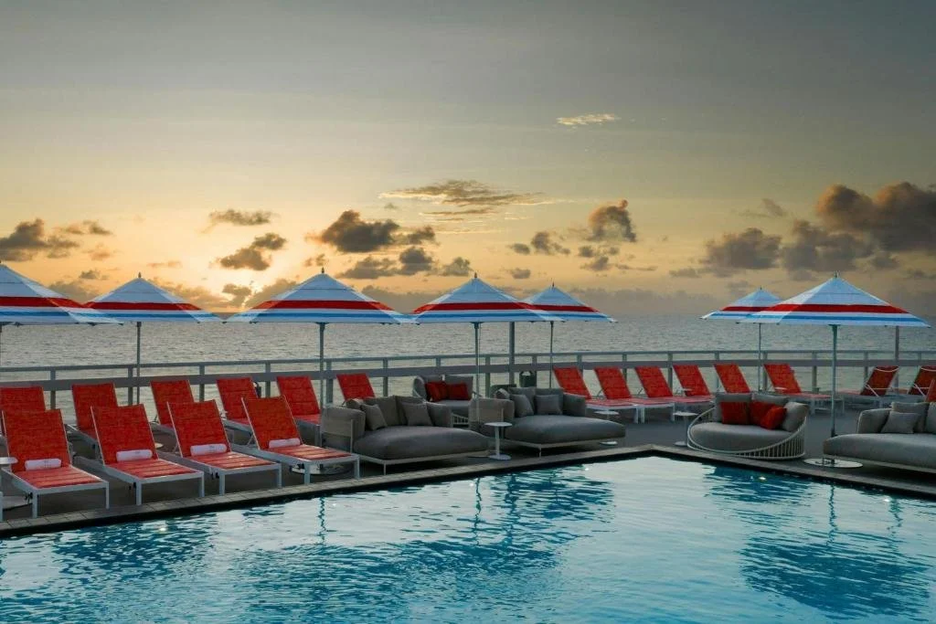 W Fort Lauderdale rooftop pool deck with red lounge chairs and red-and-white umbrellas over the Atlantic Ocean at sunset