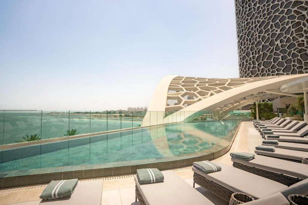 Rosewood Doha Doha cantilevered infinity pool with sun loungers beside the coral-inspired perforated tower facade and panoramic view across the Arabian Gulf