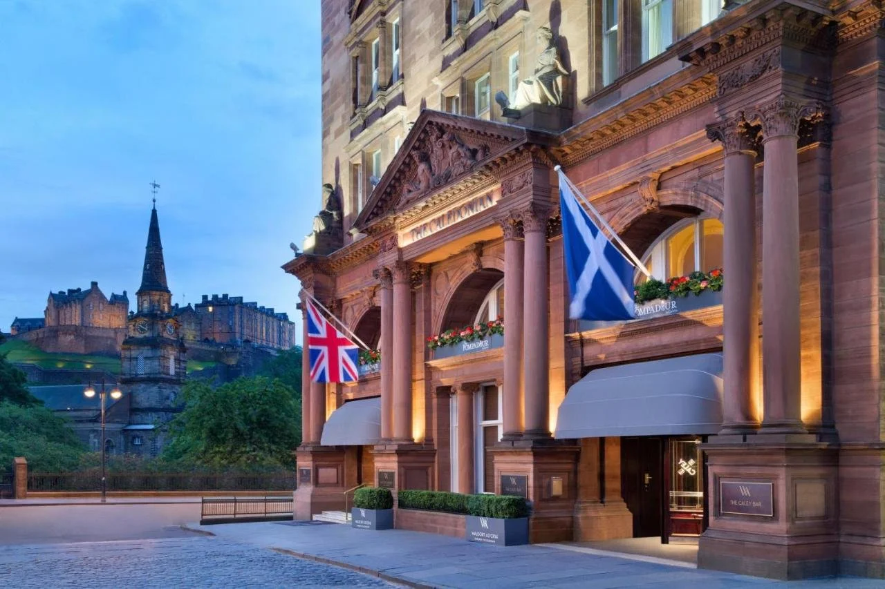 The Caledonian Edinburgh Curio Collection by Hilton hotel facade at dusk with Edinburgh Castle and Scottish Saltire flag