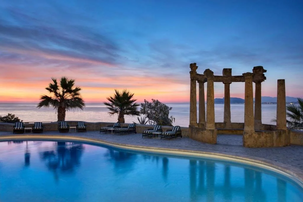 Villa Igiea Palermo pool at dusk with neoclassical stone colonnade and Bay of Palermo at sunset