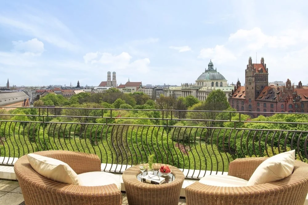 The Charles Hotel Munich upper-floor terrace with wicker chairs overlooking Alter Botanischer Garten and Frauenkirche twin towers